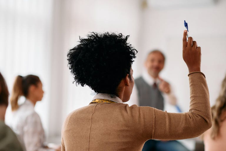 Rear view of black student raising her hand to answer a question during a class at lecture hall.