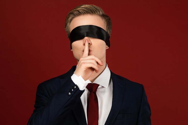 man imitating politician with blindfold on eyes showing shh gesture on red background