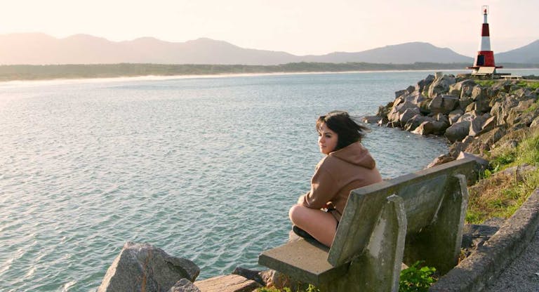 Girl sitting on bench by sea