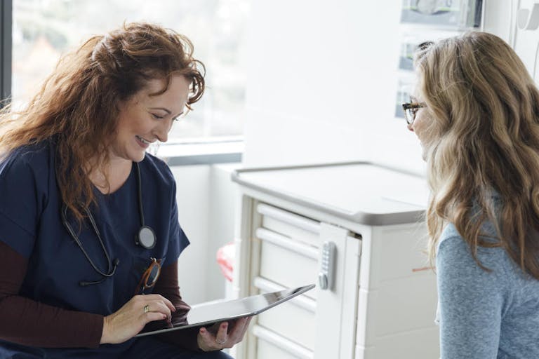 Smiling female nurse using digital tablet while talking to teenage patient in clinic