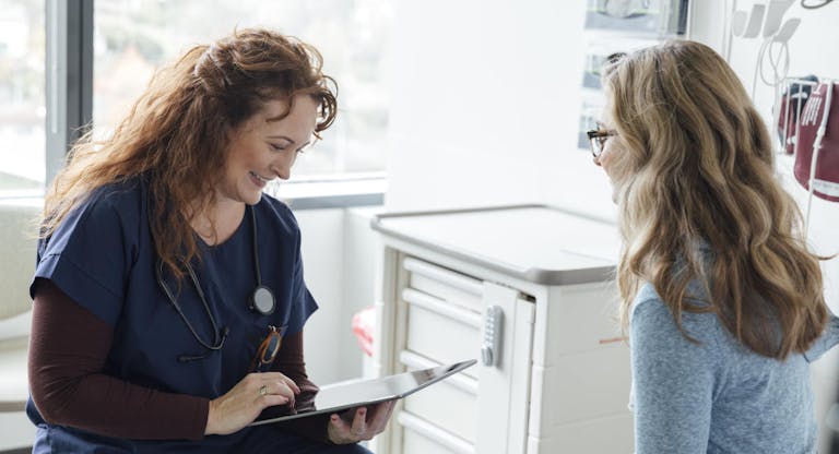 Smiling female nurse using digital tablet while talking to teenage patient in clinic