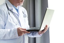 Photo: Getty Images man in white doctor's coat with stethoscope looking at laptop