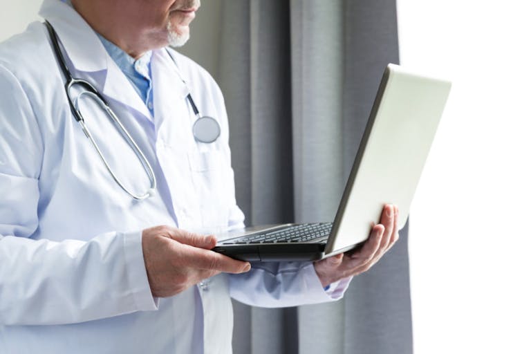 Photo: Getty Images man in white doctor's coat with stethoscope looking at laptop