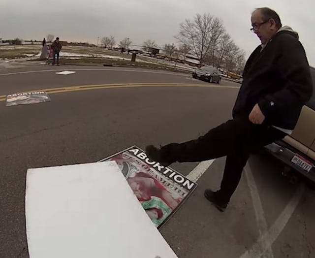 Man kicks pro-life signs onto the road in front of oncoming traffic.