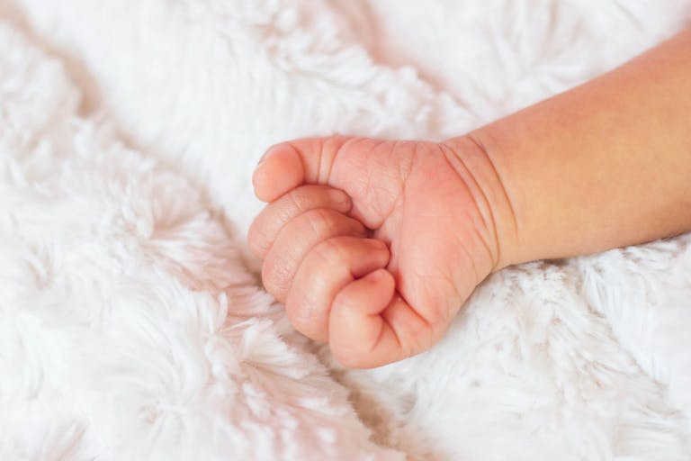 Close-Up Of Baby Hand On Bed