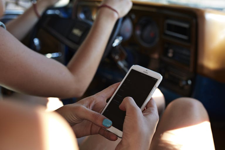 Hands of passenger scrolling on phone inside car