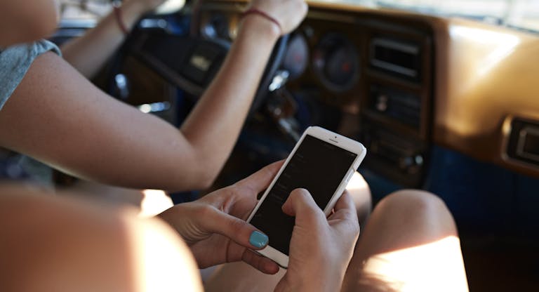 Hands of passenger scrolling on phone inside car