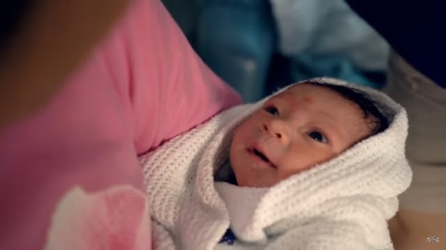 Grandmother holding her newborn grandson in screenshot from the video.