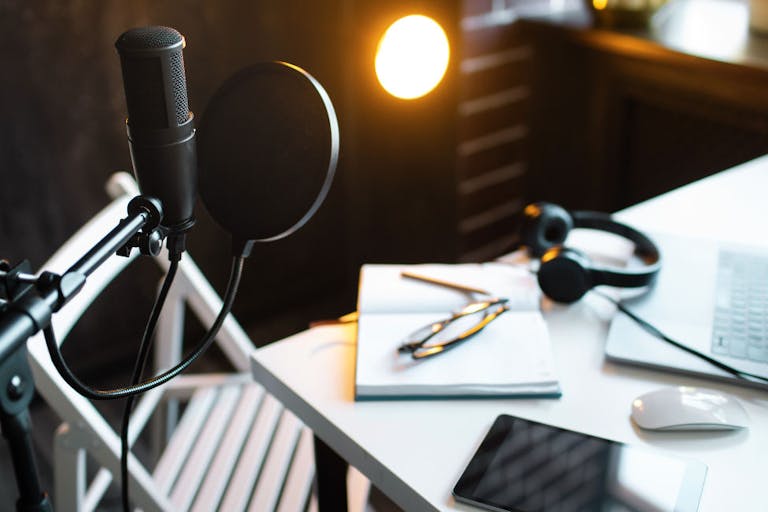 Podcast streaming at home. Audio studio with laptop, microphone with pop filter and headphones on white table against black wall with warm lights. Blogger concept.