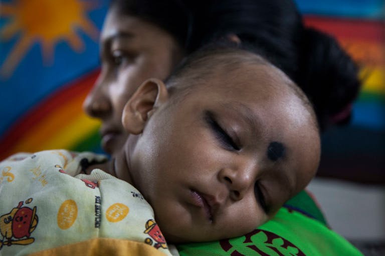 A mother holds a young child at a clinic in the Fakir Bagan