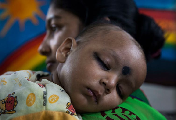 A mother holds a young child at a clinic in the Fakir Bagan