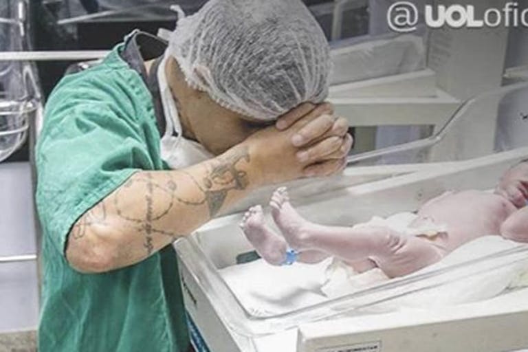Man kneels in prayer by newborn son