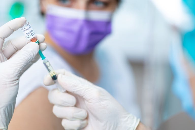 Doctor’s hands in surgical gloves preparing COVID-19 vaccine for female patient
