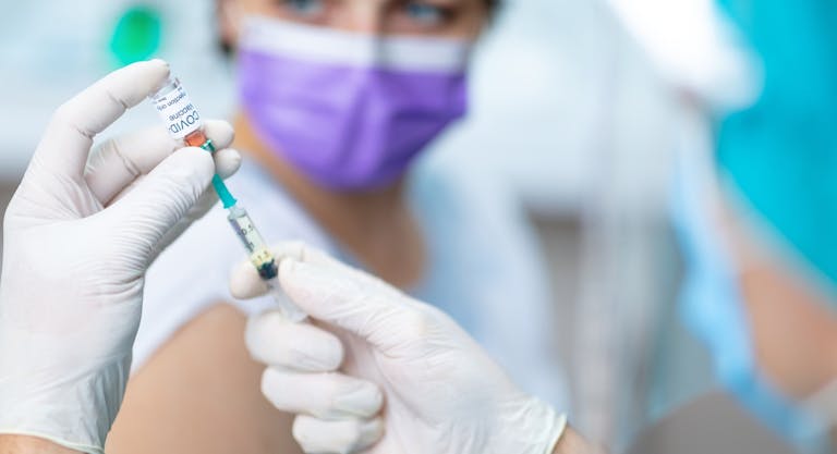Doctor’s hands in surgical gloves preparing COVID-19 vaccine for female patient