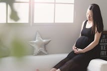 A pregnant Asian woman cradles her belly while sitting