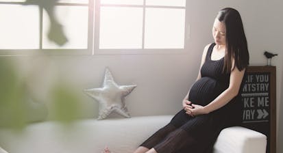 A pregnant Asian woman cradles her belly while sitting