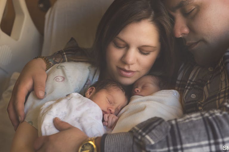 Premature Newborn Fraternal Twins Snuggle Up Together With Parents in Hospital Bed