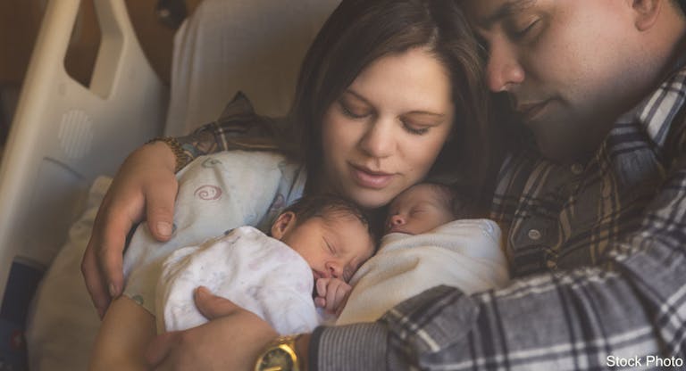 Premature Newborn Fraternal Twins Snuggle Up Together With Parents in Hospital Bed