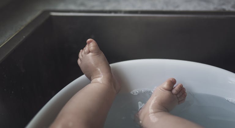 Low section of wet baby boy lying in bathtub at home