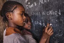 Photo: Getty Images Young African girl writing words on school chalkboard
