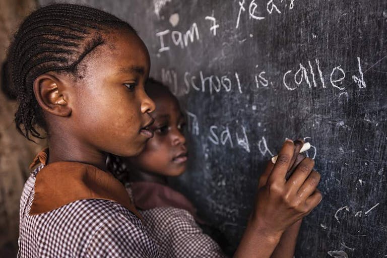 Photo: Getty Images Young African girl writing words on school chalkboard