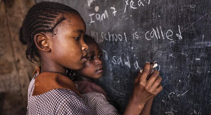 Young African girl writing words on school chalkboard