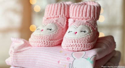 Photo shows pink baby booties on top of a pink baby blanket