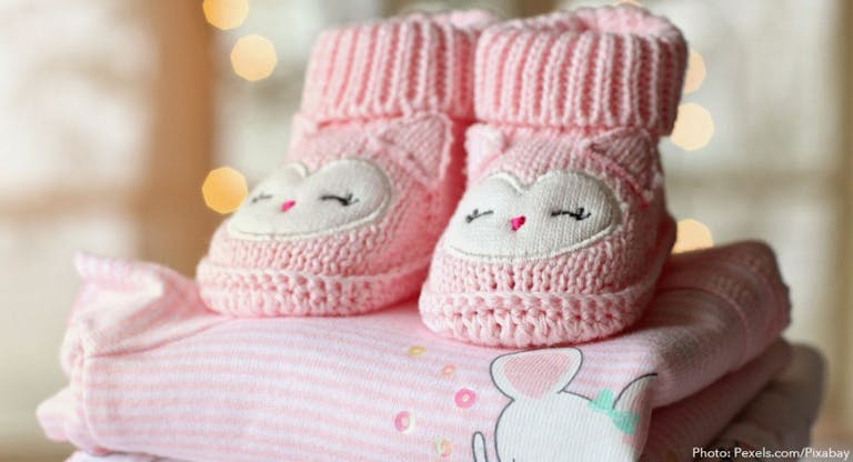 Photo shows pink baby booties on top of a pink baby blanket