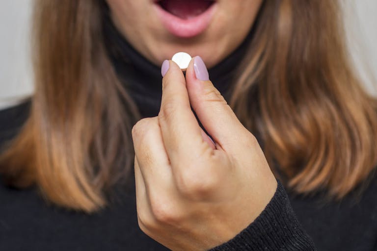 Photo: Andrii Zorii/Getty Images Young woman taking a pill. A woman takes medicine antidepressant or birth control pill, female puts tablet in mouth have painkiller or antibiotic. Healthcare concept with medicines.