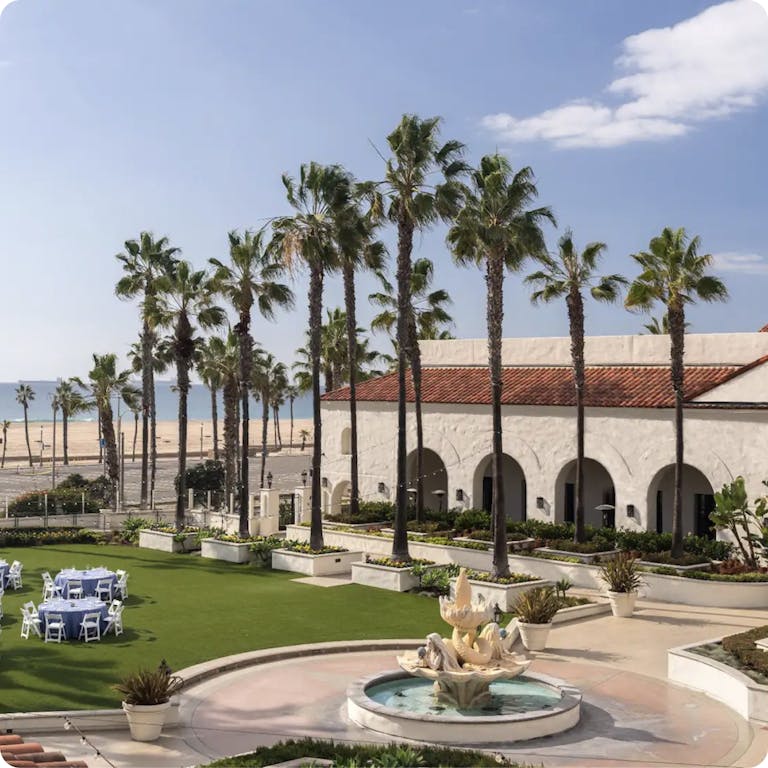 A hotel on the beach with palm trees and a fountain