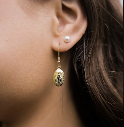 A pearl earring and a gold earring with a saint on it