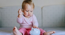 Baby girl  putting one coin into piggy bank.