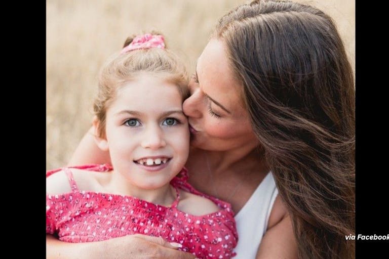 Nine-year-old Charleigh Pollock wearing a pink shirt is held by her mother, who is kissing her on the cheek.
