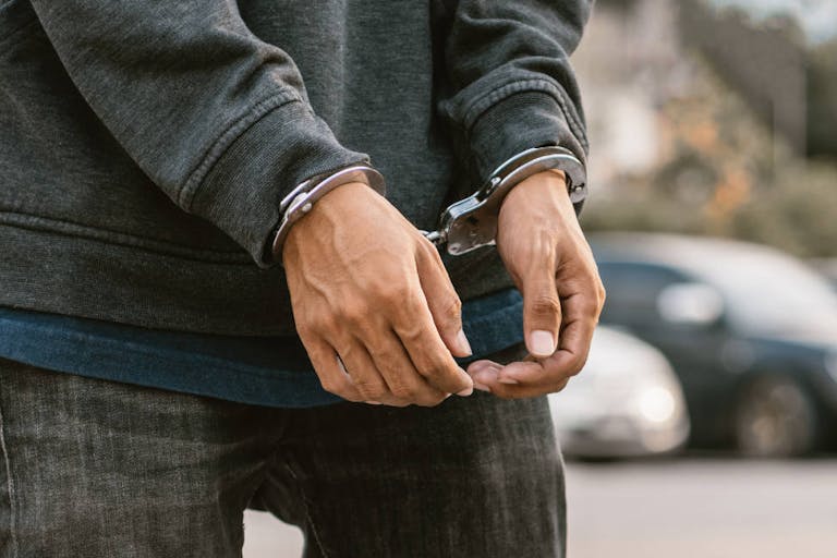Photo: Getty Images Under arrest, a man's hands with clenched fists are handcuffed behind him.