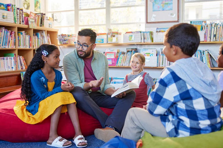 Photo: Getty Images Male teacher reading a book to students while sitting in school library. Librarian read a fairy tale to a group of multiethnic primary schoolchildren. Middle eastern man at elementary school reading stories to little boys and curious girls.