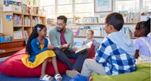 Teacher reading book to his little students in a library