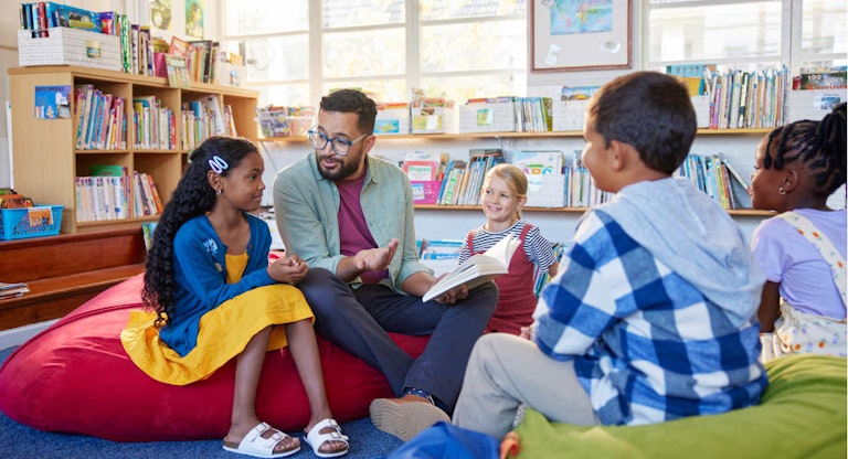 Teacher reading book to his little students in a library