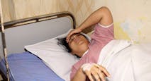 Indian woman feeling sick and suffering from a headache, lying down on the patient bed in the hospital and taking a rest.