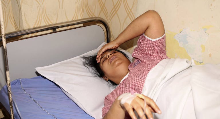 Indian woman feeling sick and suffering from a headache, lying down on the patient bed in the hospital and taking a rest.
