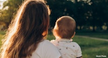 mother with curly hair holding a baby in her arms in the park in the sunset light
