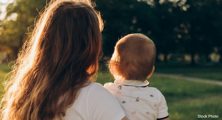 mother with curly hair holding a baby in her arms in the park in the sunset light