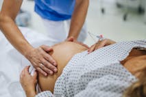 Obstetrician examining pregnant woman in hospital, touching woman’s belly, examine position of baby, breach position, size of baby and movements. Woman in labour laying on hospital bed, talking with ob-gyn doctor in maternity ward. Obstetrician examining pregnant woman in hospital, touching woman’s belly, examine position of baby, breach position, size of baby and movements. Woman in labour laying on hospital bed, talking with ob-gyn doctor in maternity ward.