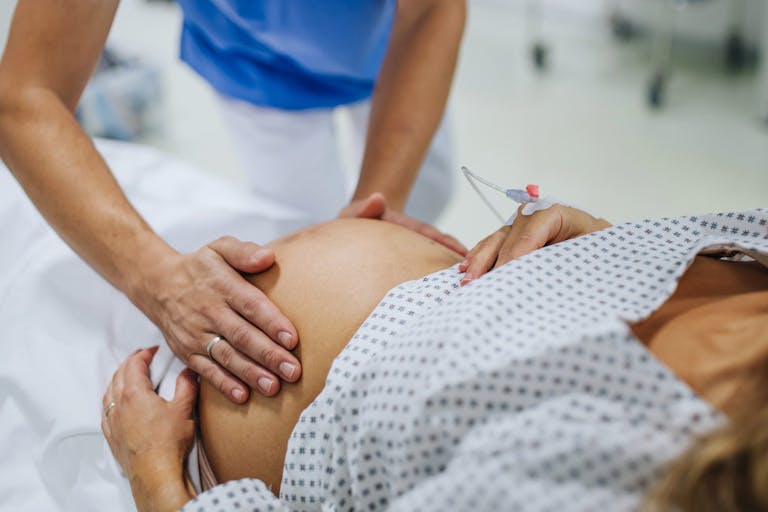 Obstetrician examining pregnant woman in hospital, touching woman’s belly, examine position of baby, breach position, size of baby and movements. Woman in labour laying on hospital bed, talking with ob-gyn doctor in maternity ward. Obstetrician examining pregnant woman in hospital, touching woman’s belly, examine position of baby, breach position, size of baby and movements. Woman in labour laying on hospital bed, talking with ob-gyn doctor in maternity ward.