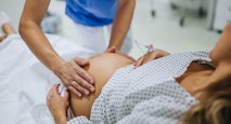 Obstetrician examining pregnant woman in hospital, touching woman’s belly, examine position of baby, breach position, size of baby and movements. Woman in labour laying on hospital bed, talking with ob-gyn doctor in maternity ward.