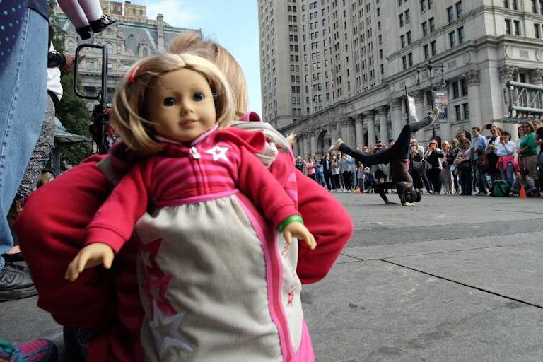 A girl with her doll peeking out of her backpack watches as a street entertainer dances during a road side show in New York on October 9, 2015. AFP PHOTO/JEWEL SAMAD        (Photo credit should read JEWEL SAMAD/AFP via Getty Images) US-STREET-ENTERTAINMENT