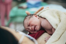 A nurse cradles a newborn baby girl in her arms, while the mother gazes lovingly at her daughter, her eyes filled with tenderness. A nurse cradles a newborn baby girl in her arms, while the mother gazes lovingly at her daughter, her eyes filled with tenderness.