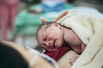 A nurse cradles a newborn baby girl in her arms, while the mother gazes lovingly at her daughter, her eyes filled with tenderness.
