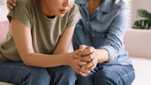 An older woman sitting next to a younger woman, holding her hand in comfort