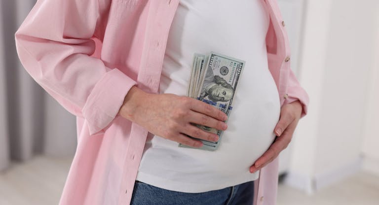 Surrogate mother. Pregnant woman with dollar banknotes indoors, closeup