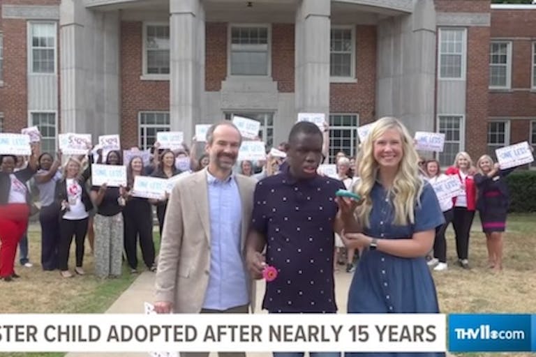 Screenshot: 11 Alive. Cozy with his parents Tim and Anna Dietrich as people behind them celebrate his adoption.